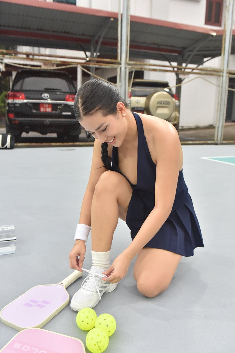 Young woman prepares for a game of pickleball by tying her sneakers on the court.